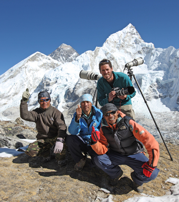 Author / Photographer Ed Darack (standing, holding camera) at 17,000 feet above sea level on Kala Patthar, beneath Mount Everest (in distance) during a photography expedition to Nepal. Copyright Ed Darack; Permission granted for use in media products about / related to Ed Darack's creative work. width=